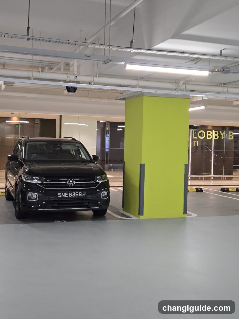 A black Volkswagen SUV is parked in an indoor parking garage next to a lime green pillar. In the background, glass doors with 'LOBBY T1' signage are visible.