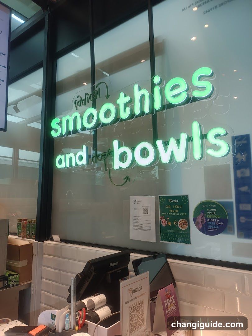 A shop front with a glass window displaying illuminated green signage reading 'smoothies and bowls'. Inside, there are posters on the wall, including one promoting 'Cafe Staff' and another encouraging customers to show their keycard for free items. A cash register is visible in the foreground along with some printed materials.