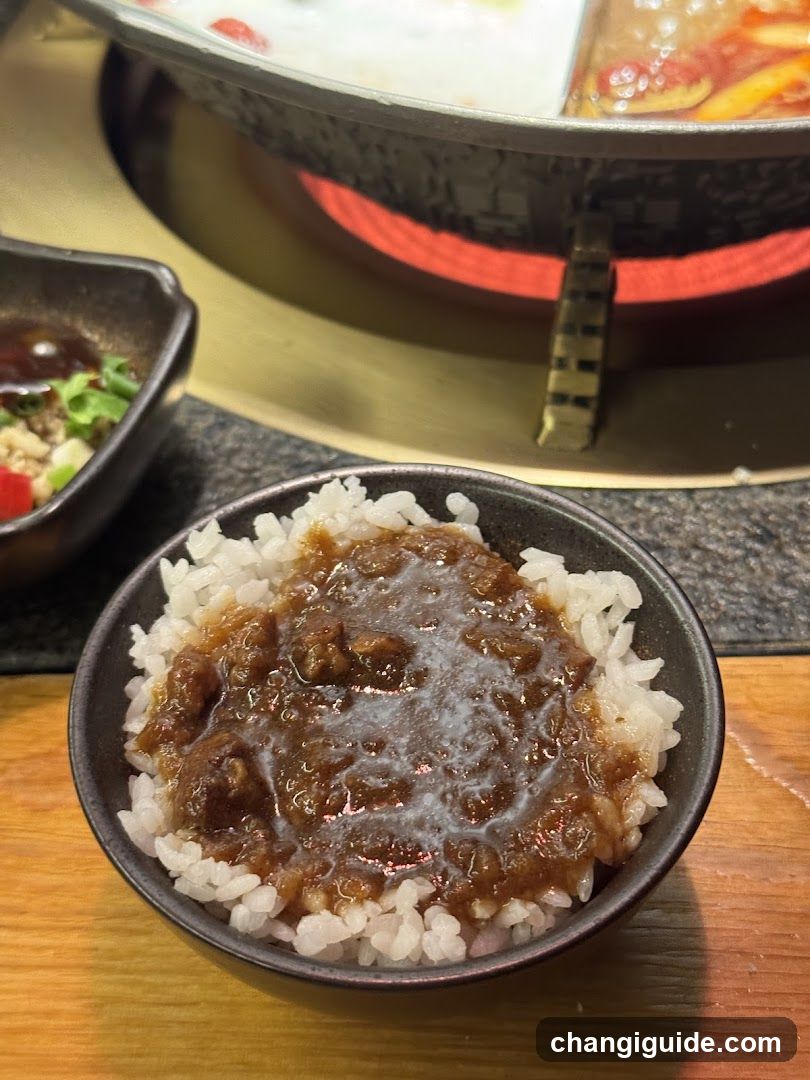 Bowl of Rice with Sauce and Hot Pot in Background