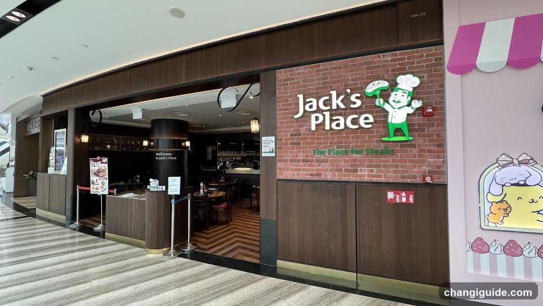 The image shows the exterior entrance of Jack's Place, a restaurant with a brick-patterned facade featuring its logo and slogan 'The Place for Steaks'. The entrance is open, revealing an interior dining area with wooden flooring and tables. A pink wall to the right displays a cartoon character illustration.
