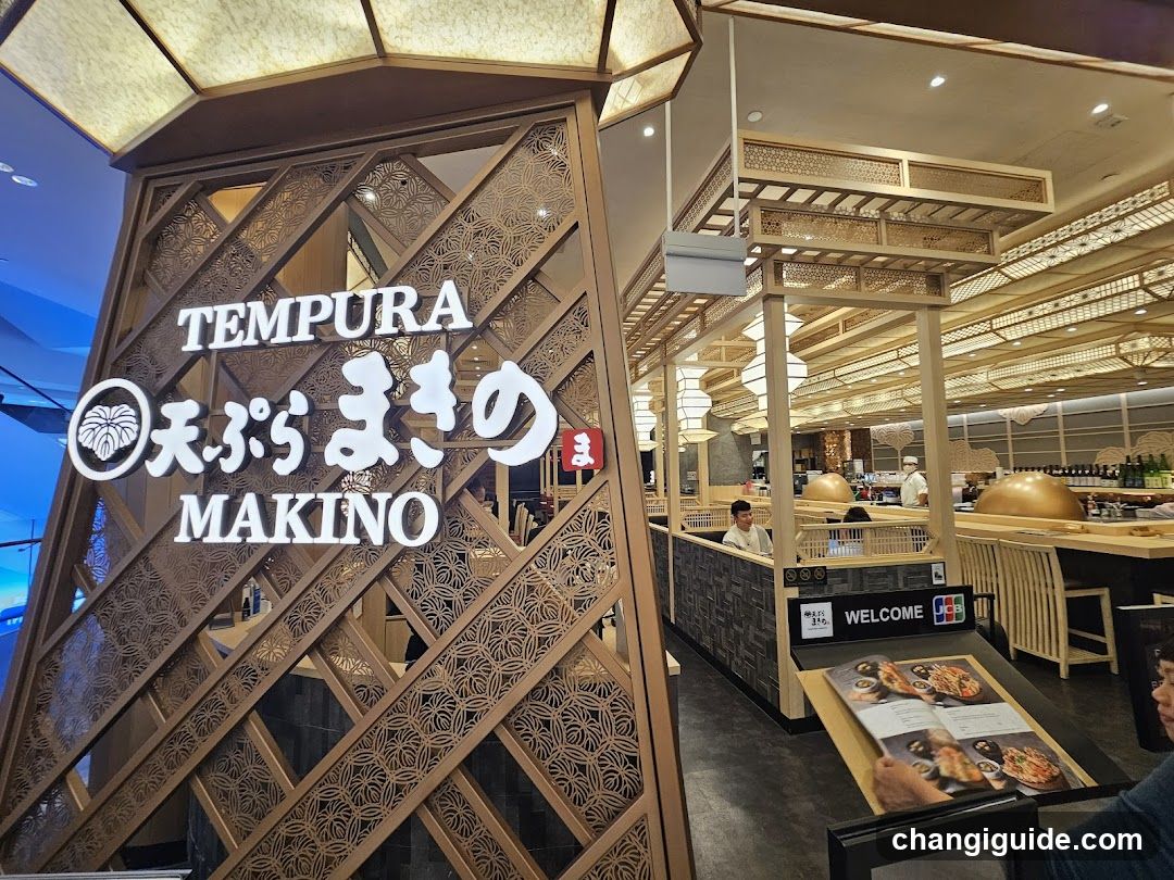 A wooden lattice entrance with illuminated signage reading 'TEMPURA' and Japanese characters, leading into a modern restaurant interior with open kitchen and dining tables.
