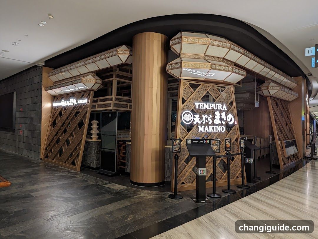 The image shows the exterior entrance of a Tempura restaurant named 'TEMPURA MAKINO'. The facade features traditional Japanese architectural elements, including wooden lattice screens and illuminated lantern-style signs. A large sign displays the name in English and Japanese characters. There are welcome stands with QR codes at the entrance.