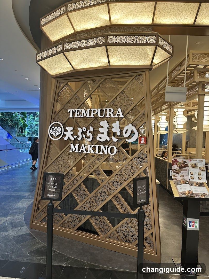A photo of the physical storefront facade of Tempura Makino, featuring a decorative wooden entrance with illuminated signage displaying 'TEMPURA' and 'MAKINO' along with Japanese characters. A queue sign directs customers to wait in line.