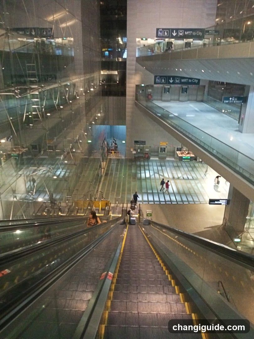 View from escalator looking up at MRT station interior with signage indicating 'MRT to City' and multiple levels of walkways.