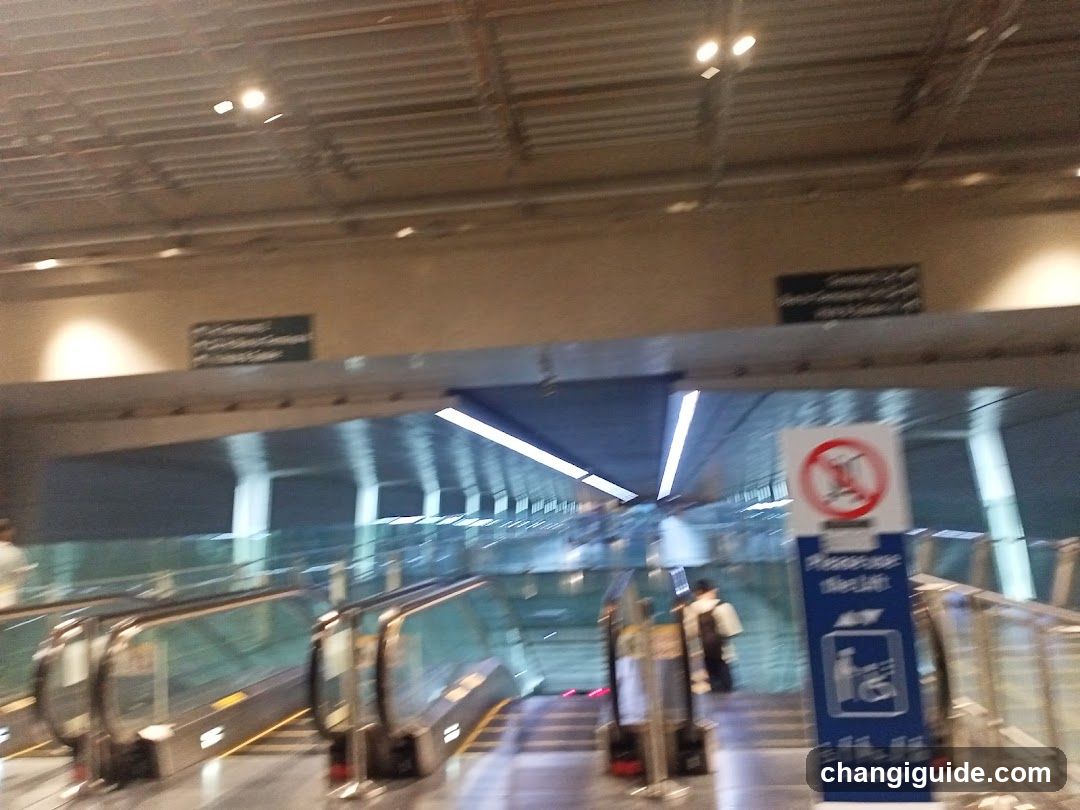 Interior view of a subway or transit station platform with escalators leading down, glass railings, and signage indicating 'Please Use Elevator' and no smoking rules. A person is visible near the elevator.