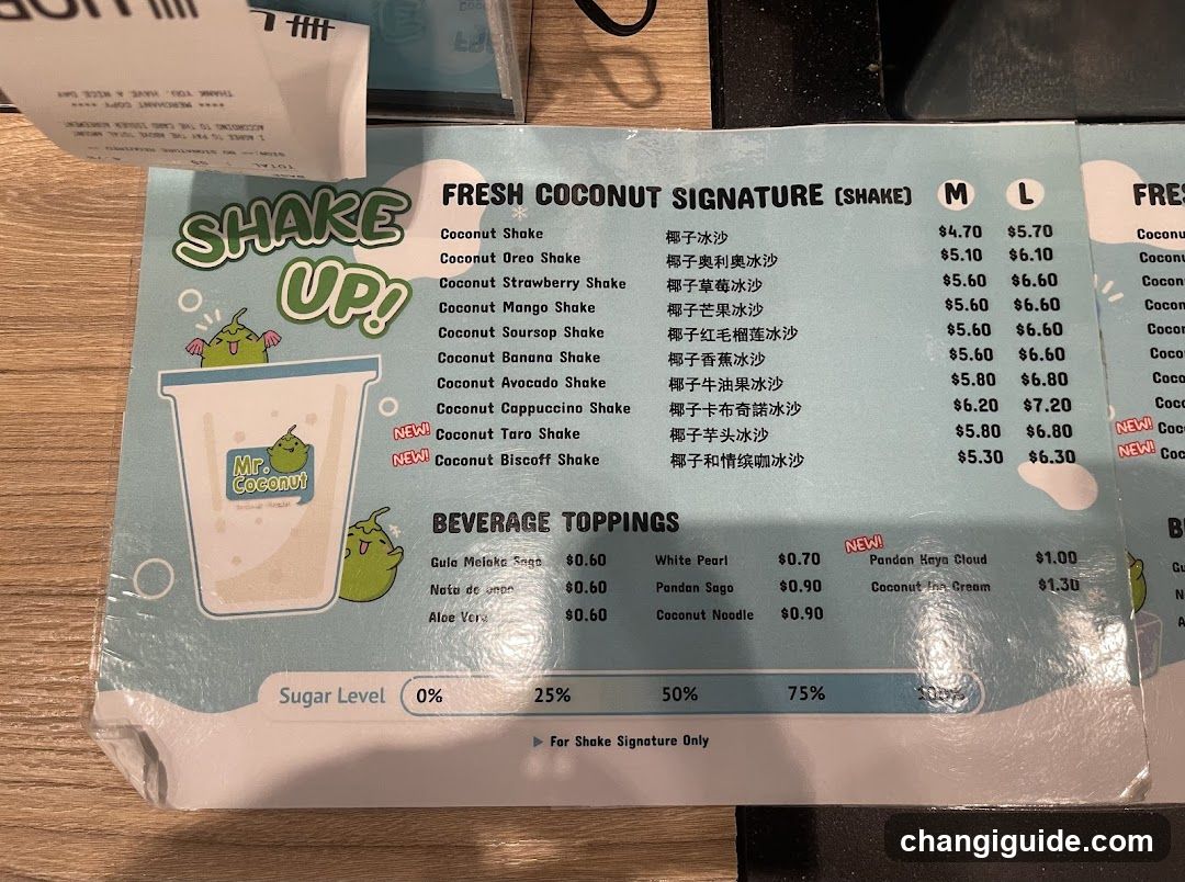 A printed menu page featuring a light blue background with green accents and cartoon illustrations of coconut-themed characters. The menu lists 'Fresh Coconut Signature' shakes in Medium and Large sizes, along with beverage toppings like Guava Melaka Sago, White Pearl, Pandan Sago, etc. A sugar level indicator is visible at the bottom.