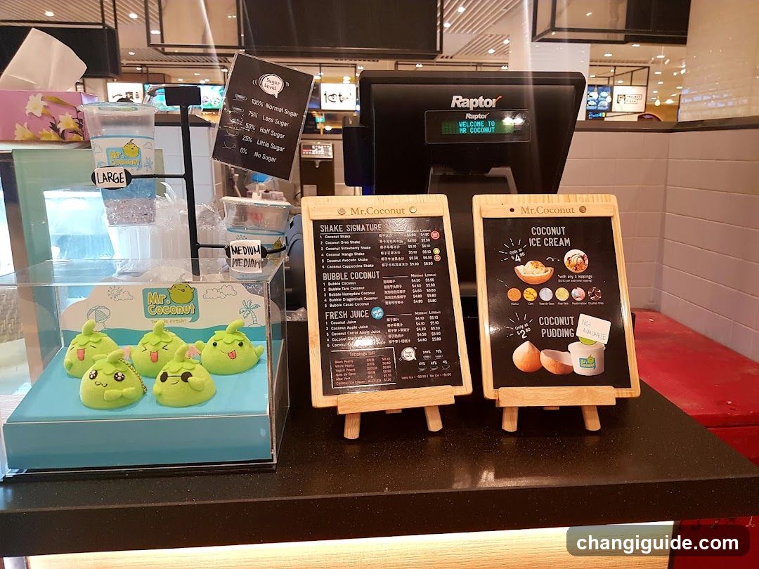 A counter display at Mr Coconut featuring green plush characters in a case, menu boards listing shakes and bubble coconut drinks, coconut ice cream options, fresh juice, coconut pudding, and a sign indicating sugar levels.