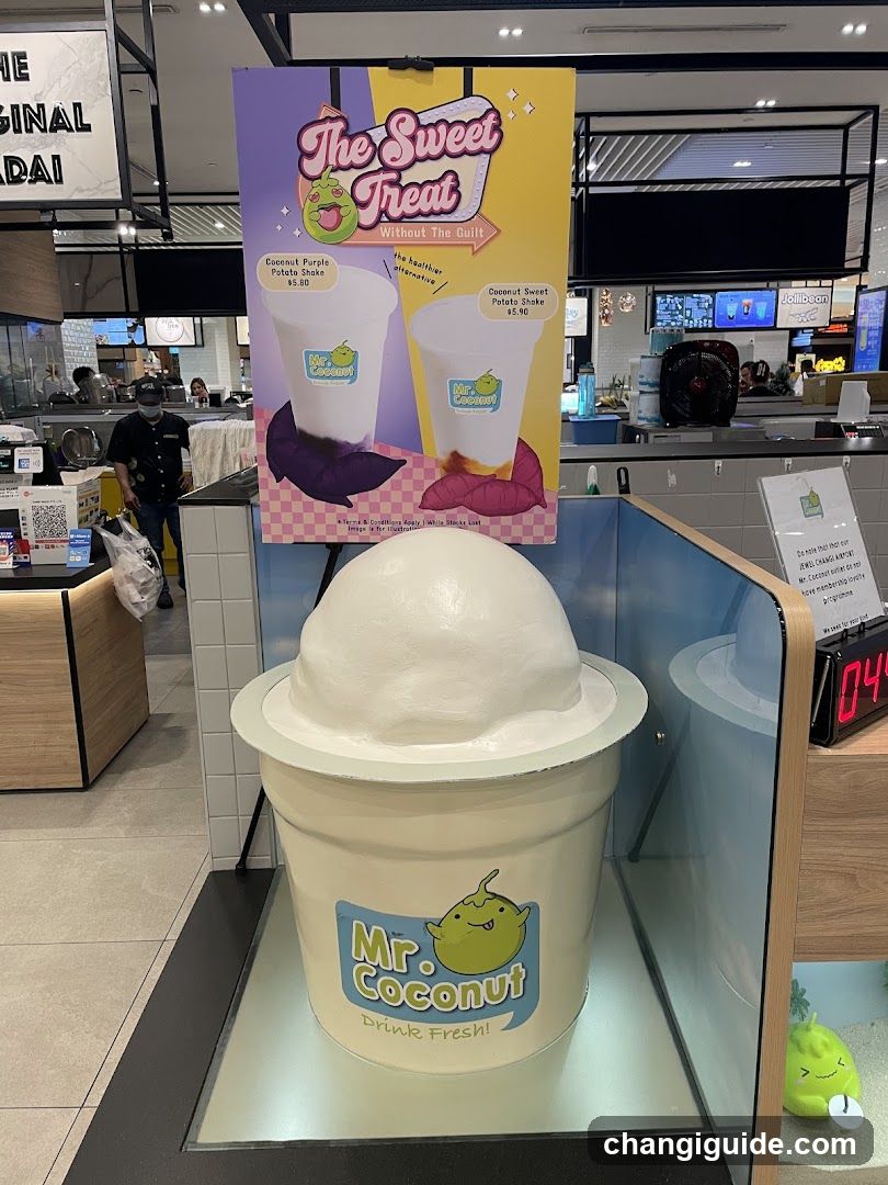 A promotional display featuring a large model of Mr. Coconut's drink cup with 'The Sweet Treat Without The Bait' poster above it, showing two drink options priced at $6.50 and $7.10 respectively.