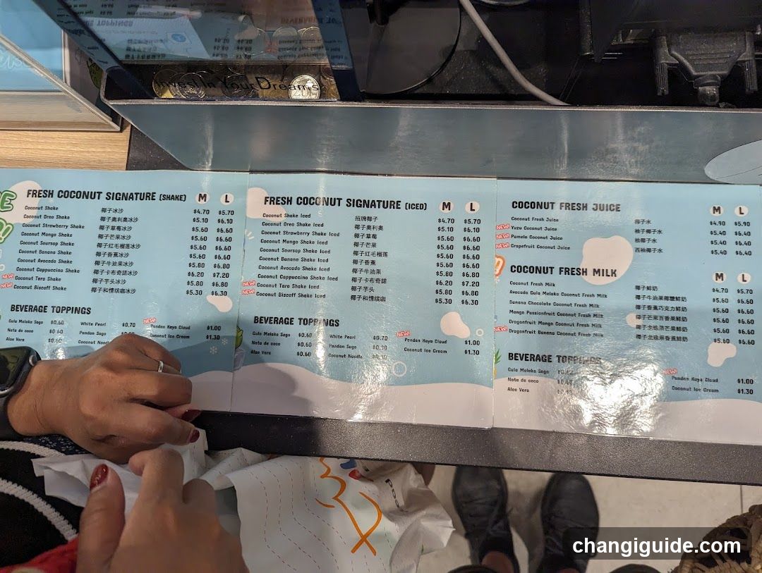 A close-up of a printed menu board featuring three columns: Fresh Coconut Signature (Shake), Fresh Coconut Signature (Iced), and Coconut Fresh Juice, with beverage toppings listed below each section.