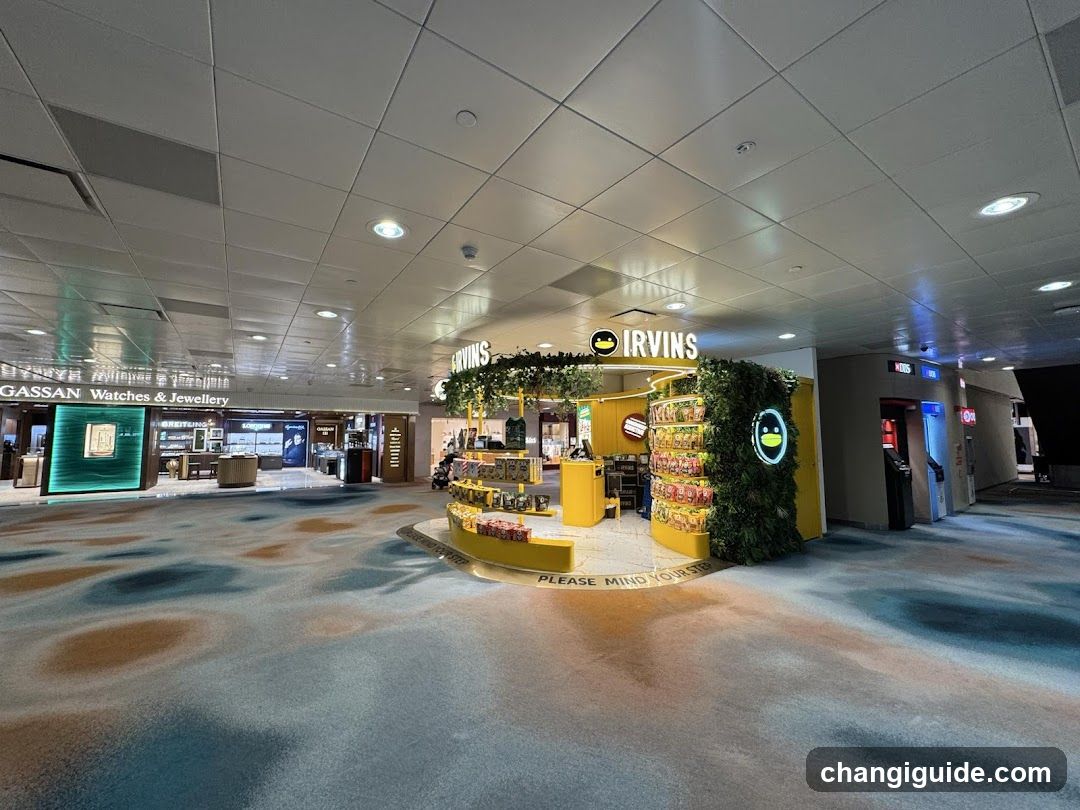 A brightly lit kiosk with yellow branding and greenery, displaying snacks and drinks. The floor has a patterned carpet, and the ceiling is tiled with recessed lighting. A sign reads 'PLEASE MIND YOUR STEP' near the entrance.