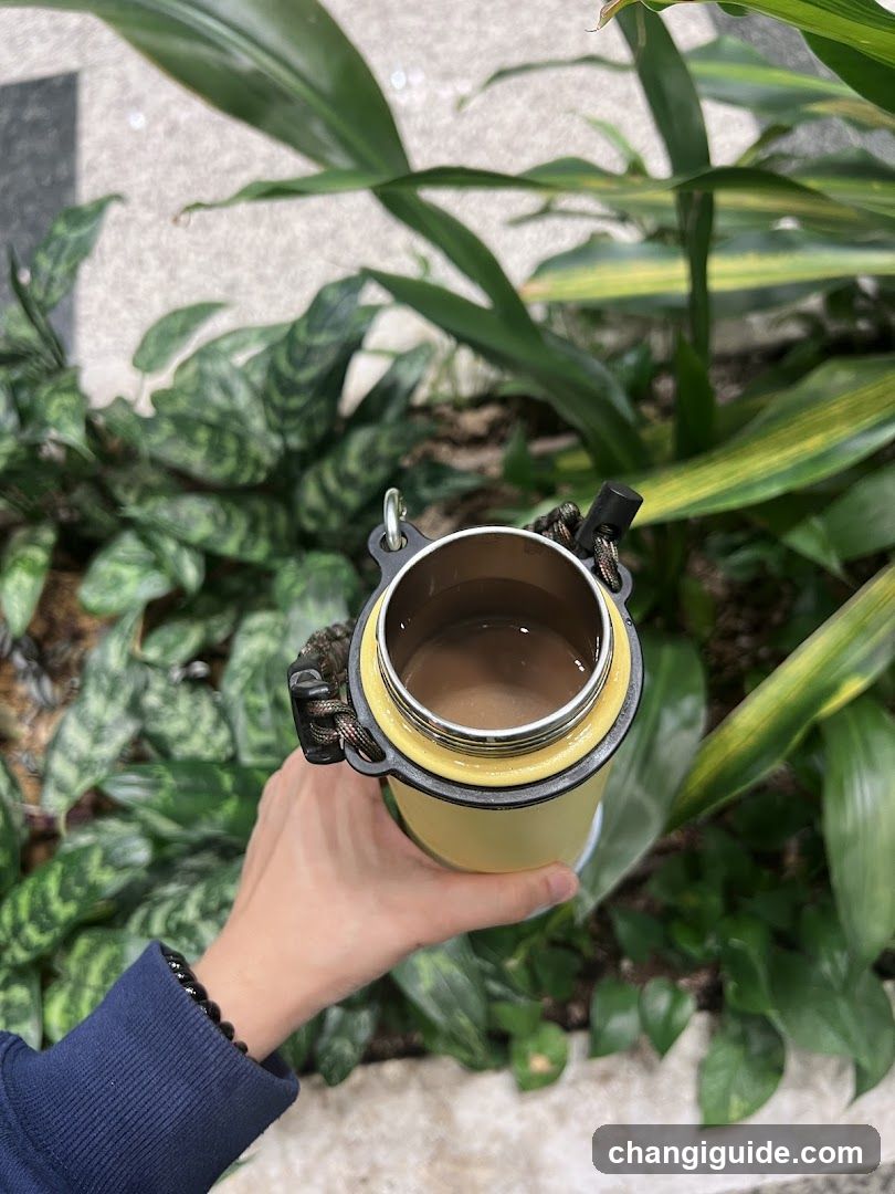 Hand holding a yellow insulated cup with plants in background