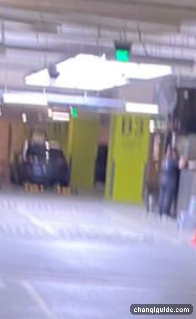 The image shows an indoor parking area or garage with a concrete floor and ceiling. There are yellow vertical structures, possibly pillars or barriers, in the background. A person is visible on the right side, standing near a wall. The lighting is artificial, coming from overhead fixtures. No shop signage or menu boards are present.