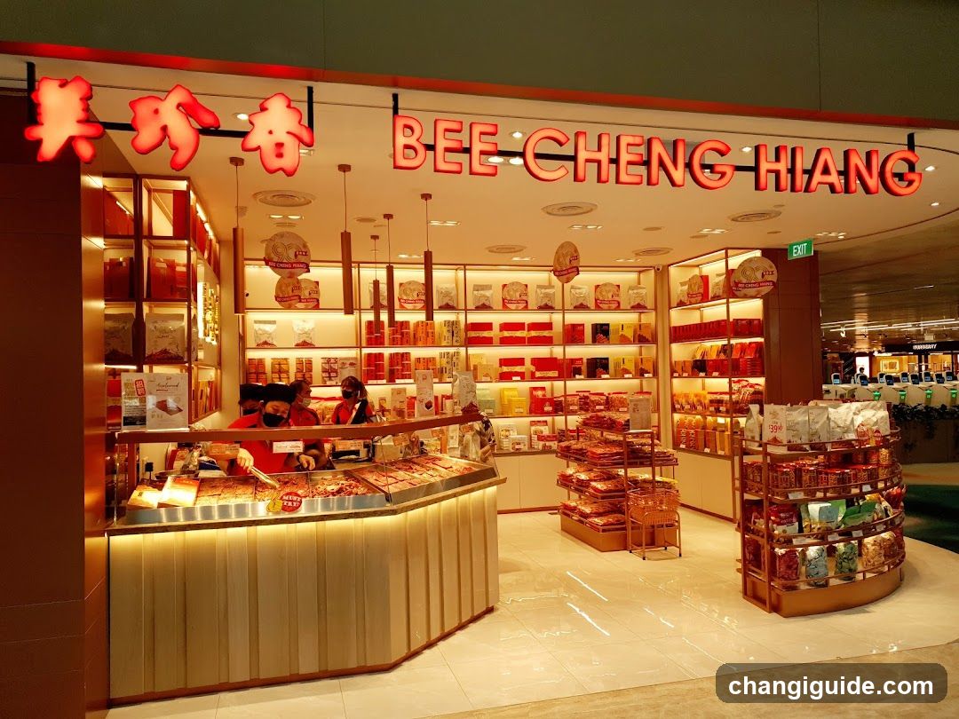 A brightly lit storefront of Bee Cheng Hiang, featuring prominent red signage with both Chinese characters and English text. The shop displays an array of packaged products on shelves, including dried goods and snacks. Inside, staff members are visible behind the counter, which is stocked with various food items under glass display cases. The interior is warmly illuminated, highlighting the organized merchandise.