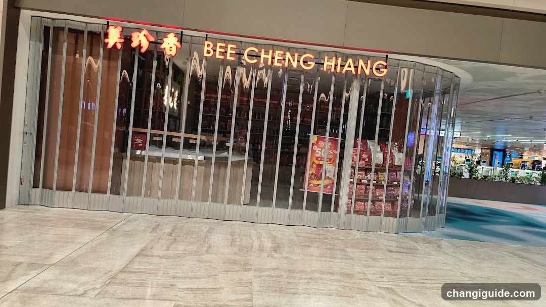 The image shows the exterior of a shop named BEE CHENG HIANG, with its name displayed in both English and Chinese characters on the facade. The store has a modern design with vertical slats covering most of the front, allowing some visibility into the interior where shelves stocked with products can be seen. There are promotional posters visible inside.
