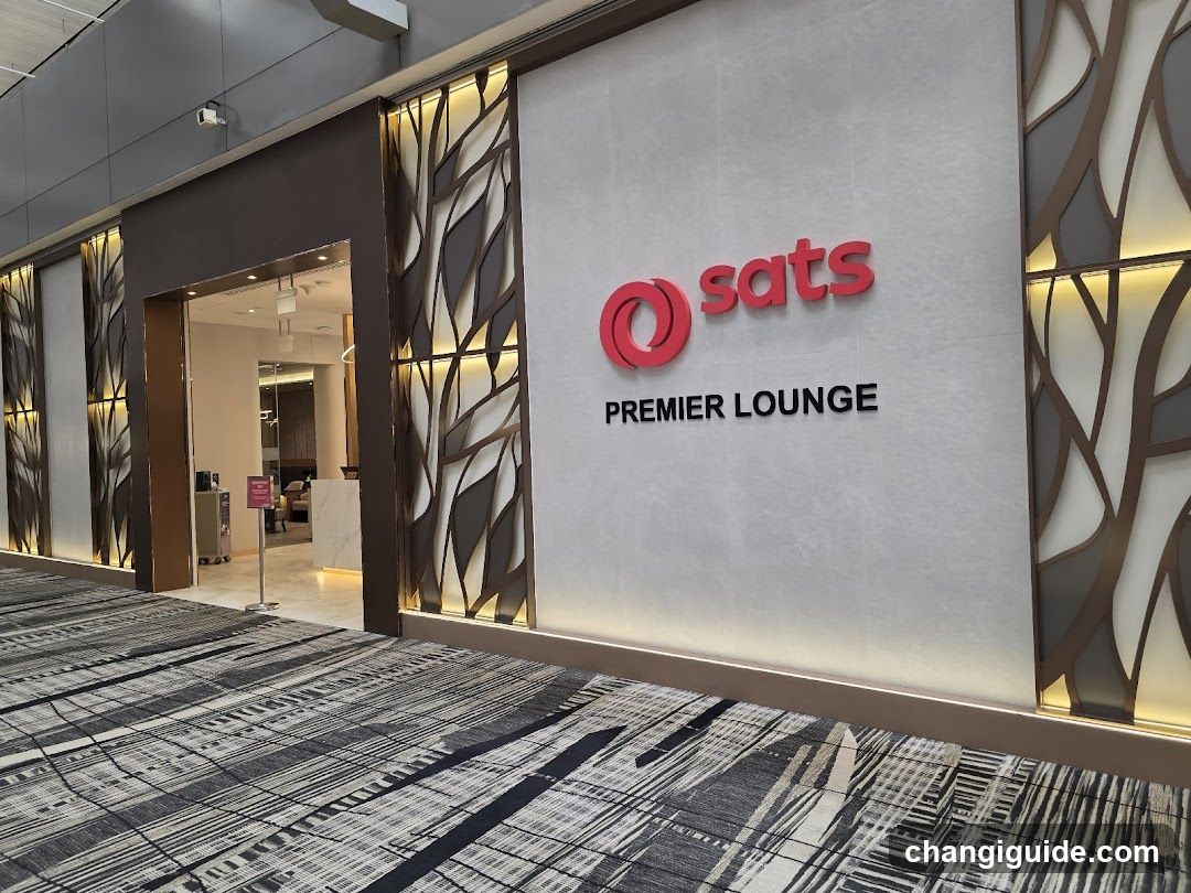 Exterior view of SATS Premier Lounge entrance featuring modern architectural design with decorative leaf-patterned panels and illuminated signage on a light gray wall.