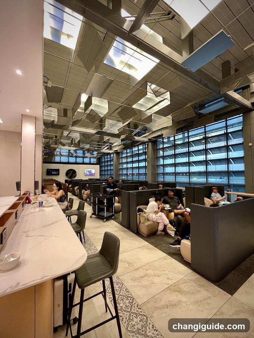 A modern airport lounge with high ceilings, exposed ductwork, and large windows showing an aircraft outside. Patrons are seated at a long counter on the left and in booth-style seating areas on the right. A service cart is visible near the center.
