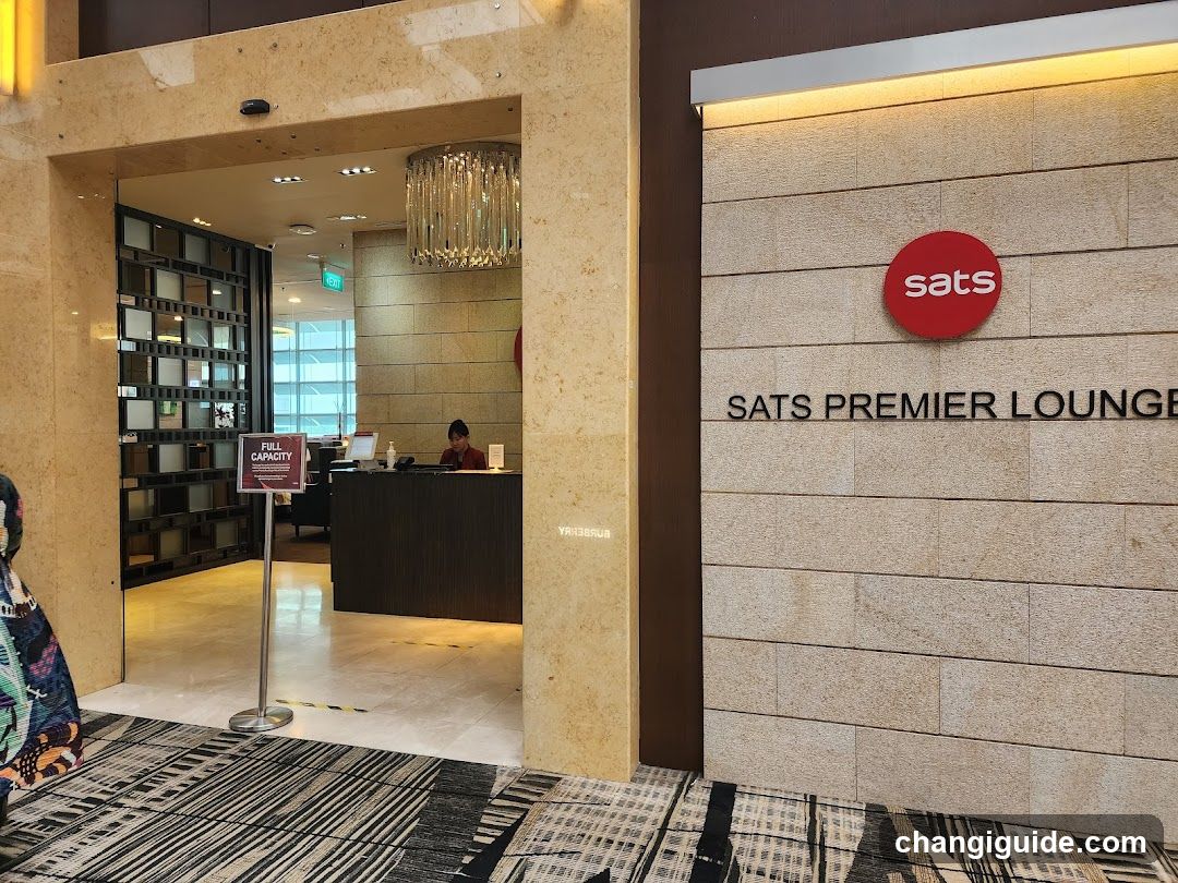 Photo of the physical entrance to SATS Premier Lounge, showing a reception desk inside and signage on the building facade.