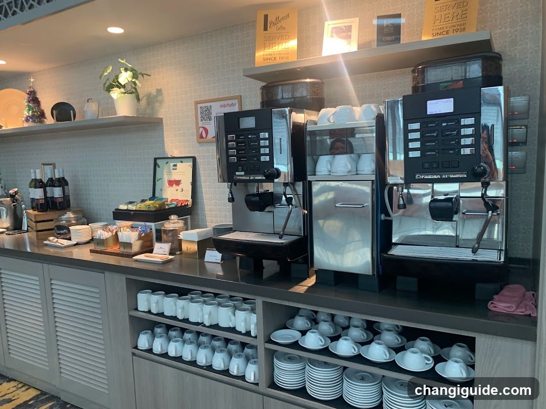 A well-lit coffee bar featuring three espresso machines, neatly stacked white cups and saucers below the counter, a small Christmas tree decoration on the shelf, and various condiments and snacks displayed in glass jars.