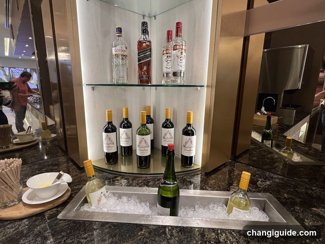 A well-lit bar display featuring shelves of liquor bottles including Gordon's Gin, Johnnie Walker Red Label, Smirnoff Vodka, and various wines. Below the shelves is a metal ice bin containing chilled wine bottles on ice. The setting appears to be an upscale lounge or hotel bar area.