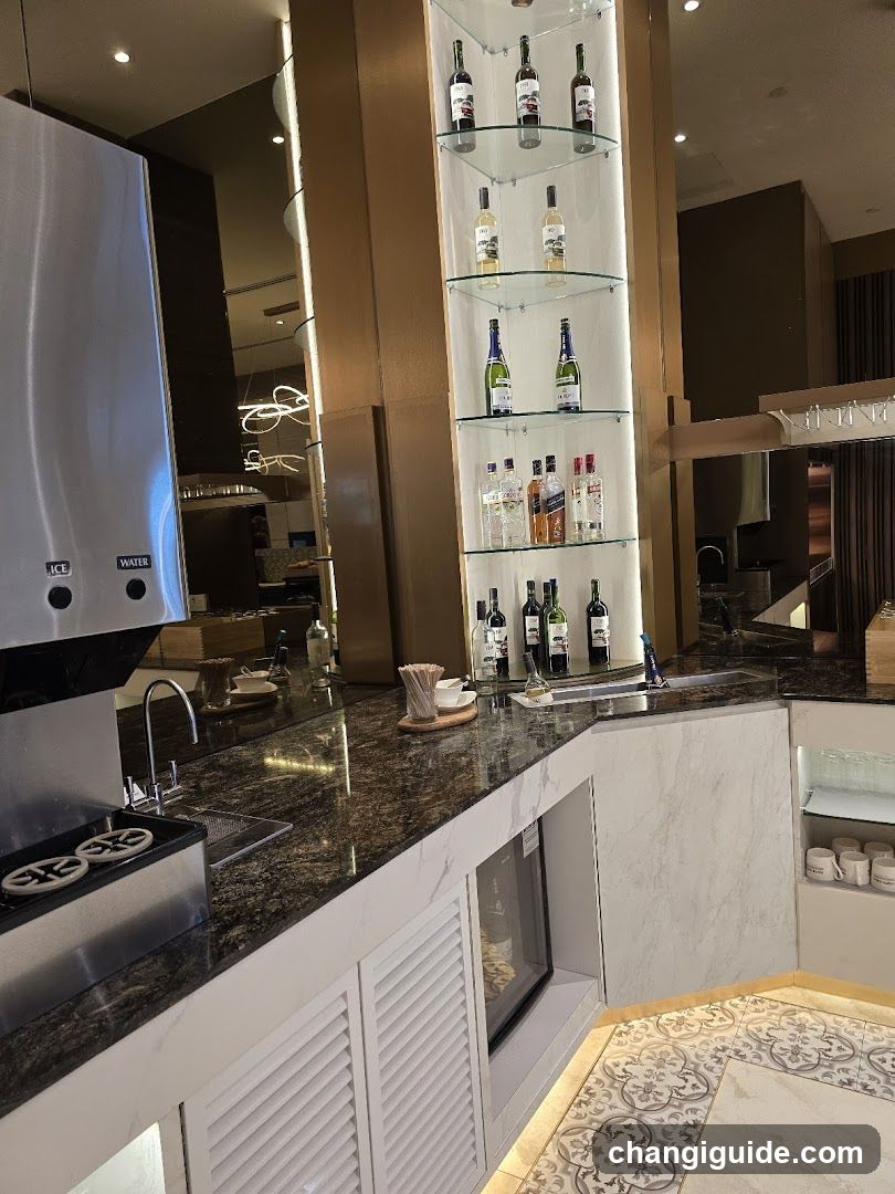 A modern bar interior featuring a sleek granite countertop, a water dispenser on the left, and a glass-enclosed wine rack displaying various bottles of alcohol. The background includes a glimpse into another room with warm lighting and decorative elements.