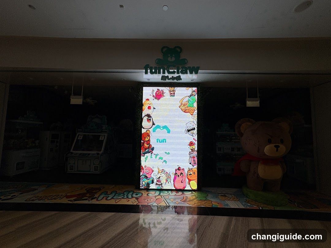 A brightly lit storefront entrance featuring a large vertical LED display showing colorful cartoon characters and the word 'fun'. Above the screen, a green sign with a bear logo reads 'FunCraw' in English and Japanese. To the right stands a life-sized brown teddy bear mascot wearing a red cape. The floor is glossy wood reflecting the scene. Inside, arcade machines are faintly visible on the left.