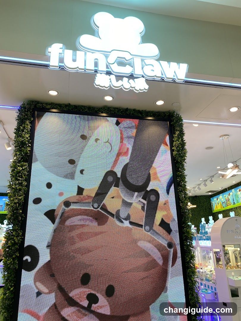 A brightly lit shop entrance with a large illuminated sign reading 'funClaw' and Japanese characters below it. A vertical LED display shows animated claw machine graphics, surrounded by greenery. Inside, claw machines are visible.