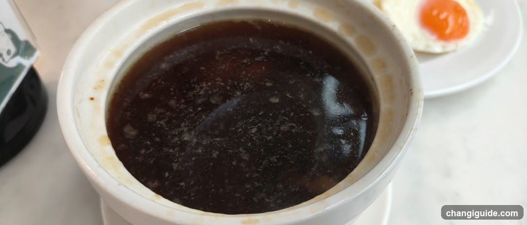 Bowl of Dark Soup with Fried Egg Side Dish