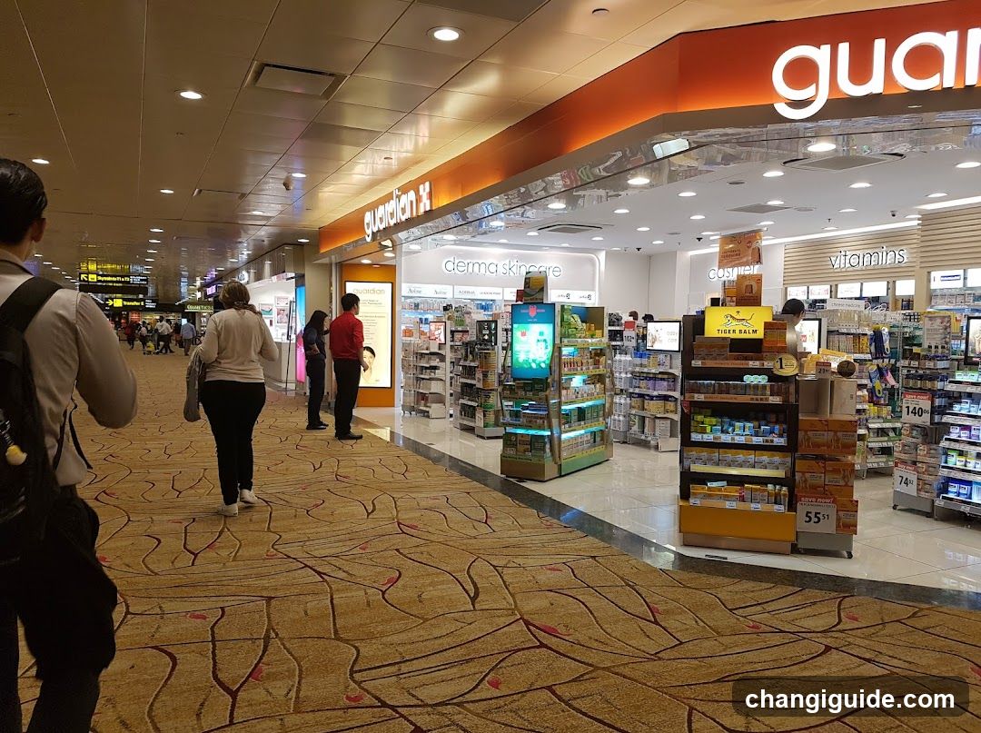 Interior shot of a Guardian pharmacy with visible signage, shelves stocked with products like derma skincare and vitamins, digital display kiosk, and customers walking through the corridor.