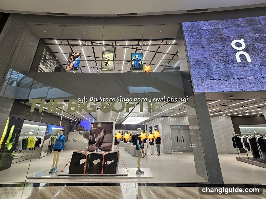 A modern retail store entrance with glass facade and visible signage reading 'THE BIG SOFT' on the window. Inside, mannequins display clothing items under bright lighting. A large screen shows a textured blue background with white letters. Star-shaped decorations are placed near the center of the display area.