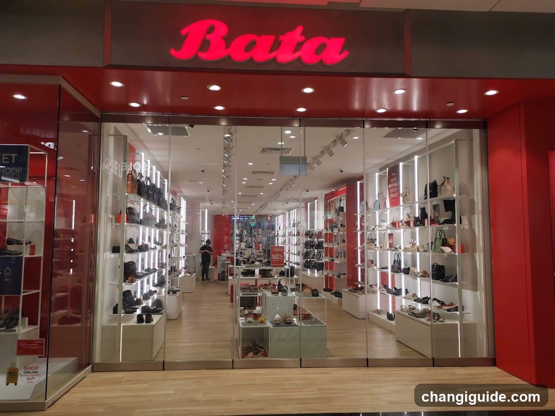 The image shows the exterior of a Bata shoe store, featuring a prominent red sign with illuminated 'Bata' lettering above glass doors. Inside, shelves display various shoes and bags under bright lighting.