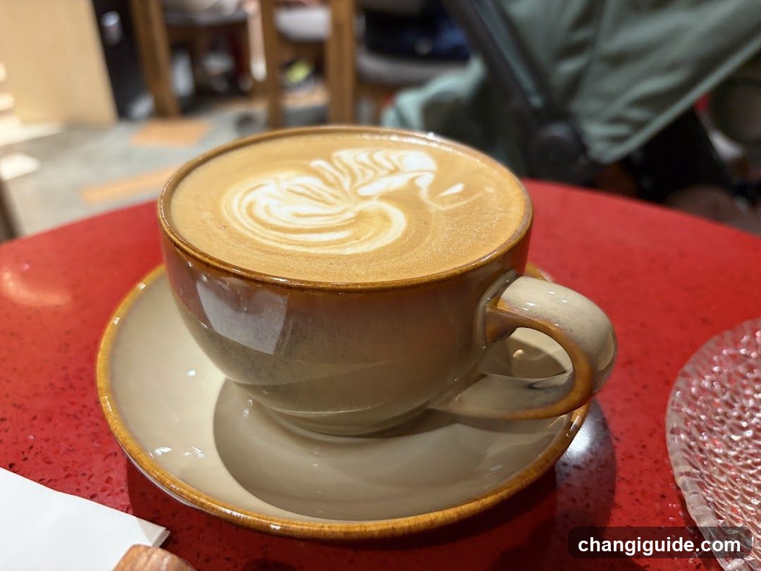 A close-up of a latte with intricate foam art in a ceramic cup on a red table.