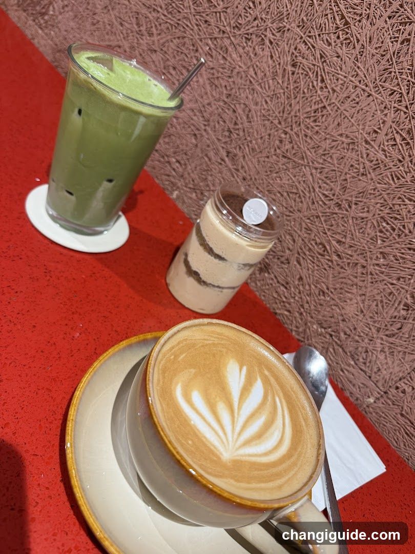 A close-up of three beverages on a red table: a latte with leaf art, a layered dessert drink, and a green matcha drink in a tall glass.