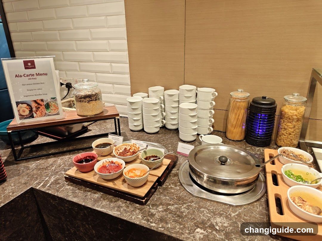 A buffet setup featuring various food items, including bowls of sauces and condiments on wooden trays, a covered metal pot, stacks of white cups, jars of pasta, and a menu board labeled 'Ala-Carte Menu'.