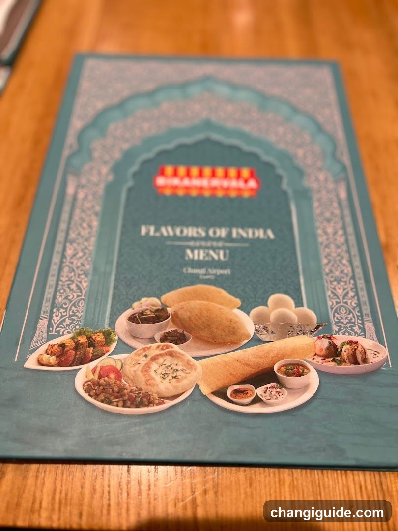 A printed menu cover featuring an arched design with the text 'FLAVORS OF INDIA MENU' and 'Changi Airport'. The cover displays images of various Indian dishes including samosas, naan breads, rice balls, and small bowls of chutneys or curries.