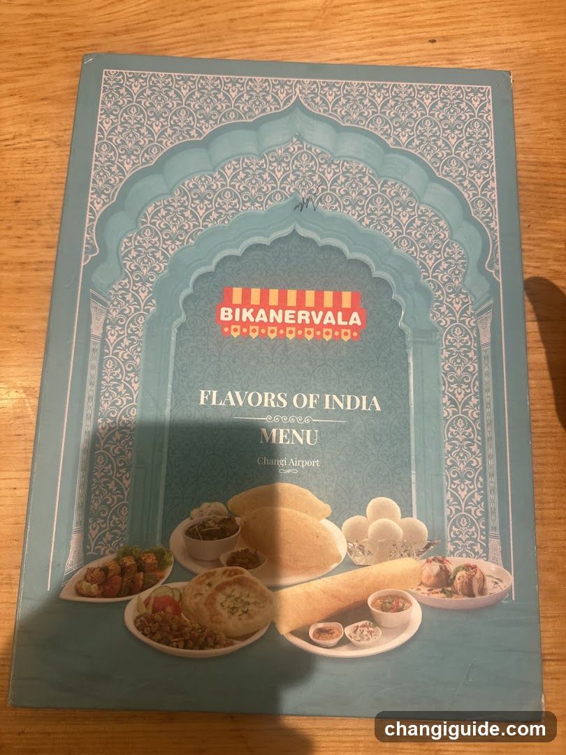 A printed menu cover featuring an ornate arch design with the Bikanervala logo and 'Flavors of India' text, showcasing images of Indian dishes like breads, curries, and sweets.