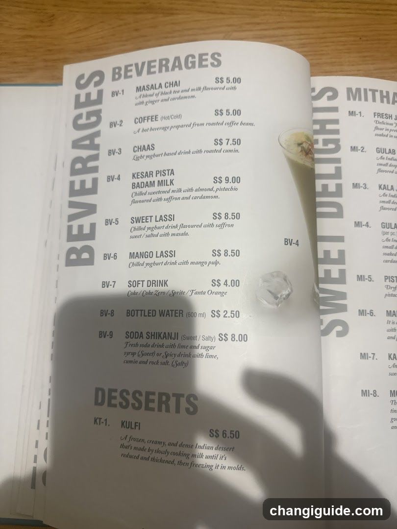 A printed menu page showing beverages (Masala Chai, Coffee, Chaas, Kesar Pista Badam Milk, Sweet Lassi, Mango Lassi, Soft Drink, Bottled Water, Soda Shikanju) and one dessert item (Kulfi), with prices in SGD.