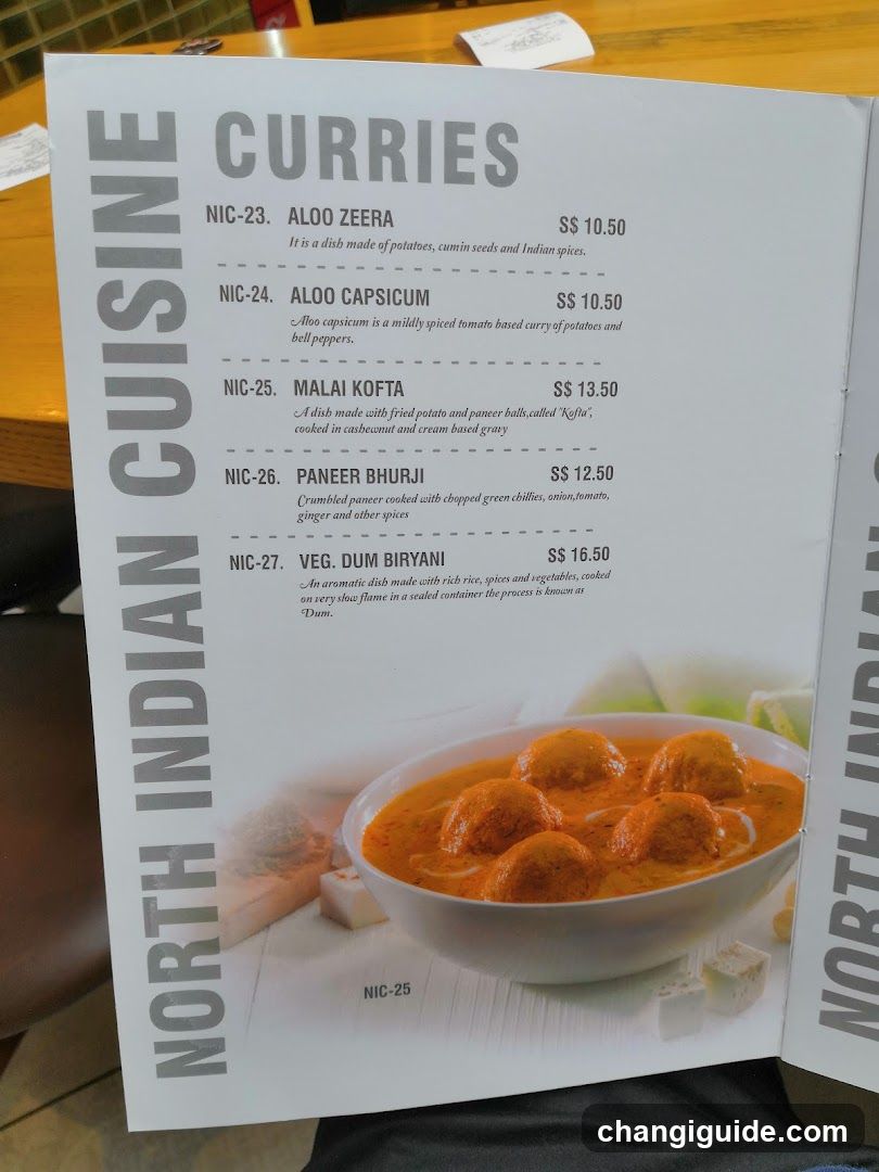 A printed menu page displaying a selection of North Indian curry dishes with descriptions and prices in Singapore dollars (S$). The section includes items like Aloo Zeera, Aloo Capsicum, Malai Kofta, Paneer Bhurji, and Veg Dum Biryani.