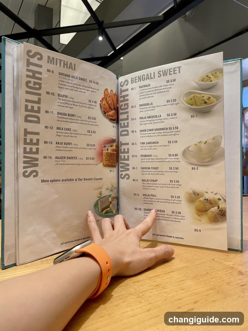 A person's hand holding an open menu displaying 'Mithai' and 'Bengali Sweet' sections with prices.