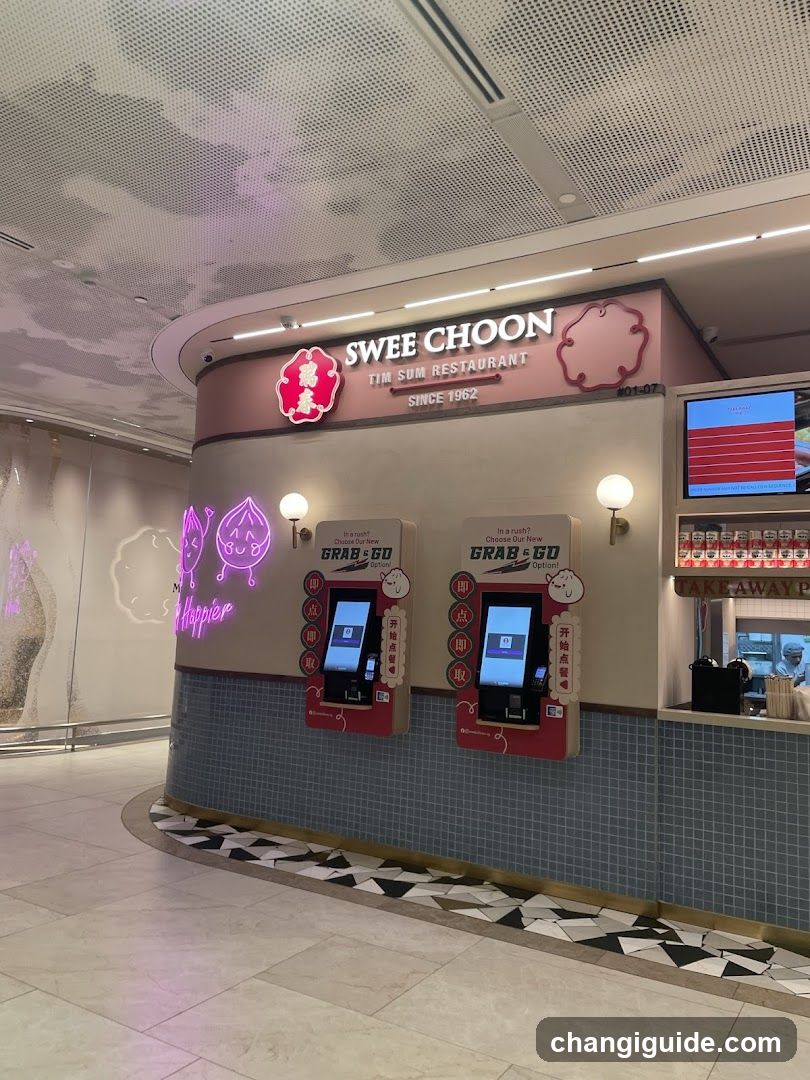 A modern storefront of Swee Choon Tim Sum Restaurant, featuring a curved facade with pink and beige tones. The sign displays 'SWEE CHOON TIM SUM RESTAURANT SINCE 1962' along with the restaurant's logo. Two Grab & Go self-service kiosks are mounted on the wall, each equipped with touch screens. A neon sign reading 'Whopper' is visible to the left, while a digital menu board is displayed above the service counter.
