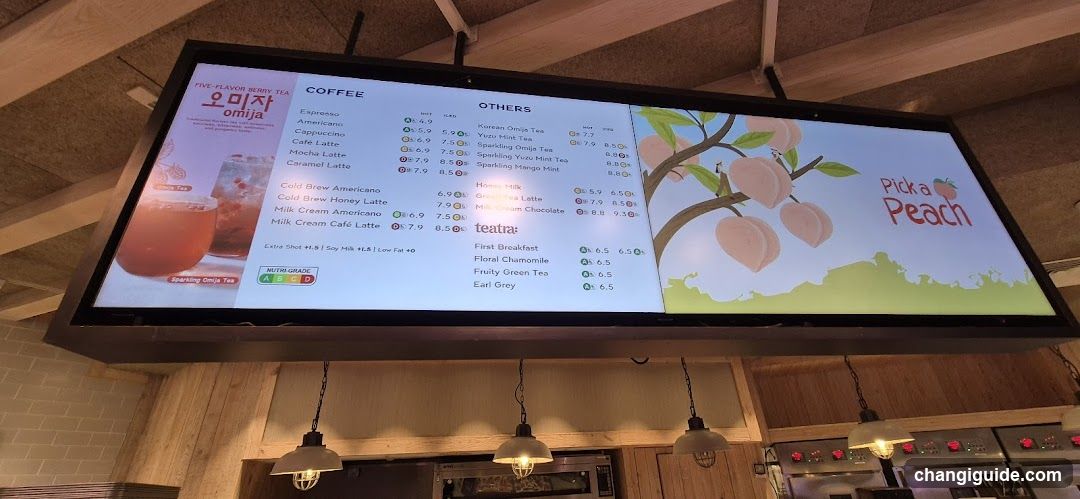A digital menu board displaying coffee, tea, and breakfast items with prices in KRW. The left side features a promotional image of 'Pick a Peach' 5-flavor berry tea. The right side shows a graphic of peaches on a tree with the slogan 'Pick a Peach'. Below are lists of drinks like Espresso, Cappuccino, Korean Oolong Tea, and others.