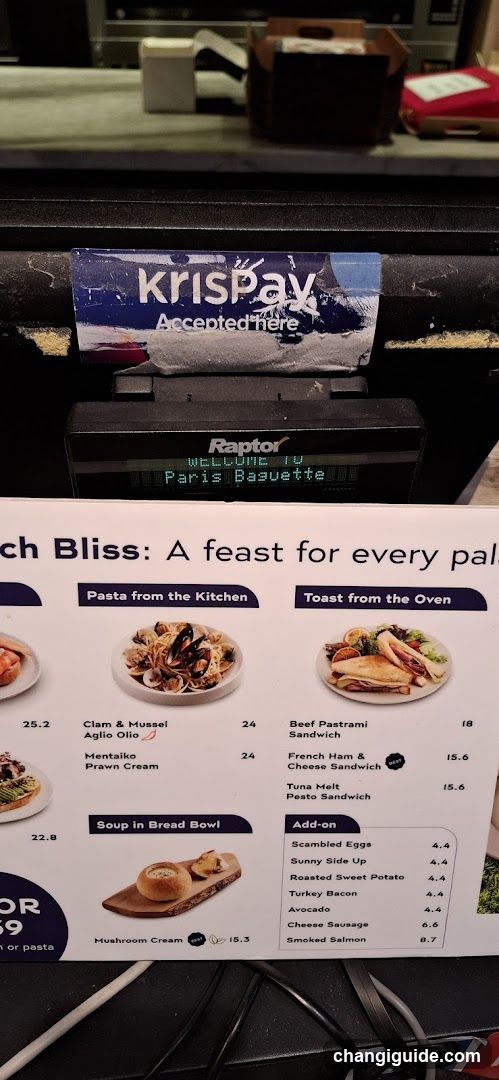A close-up of a printed menu board showing food items with prices, including pasta dishes like Clam & Mussel Aglio Olio and Mentaiko Prawn Cream, toast options such as Beef Pastrami Sandwich and French Ham & Cheese Sandwich, soup in bread bowl, and add-ons like scrambled eggs and avocado.