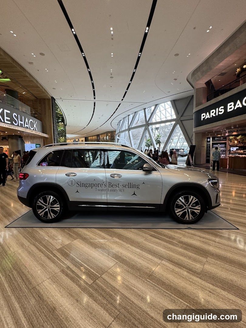A silver SUV is displayed inside a shopping mall, with visible signage for 'KE SHACK' and 'PARIS BAG' nearby.