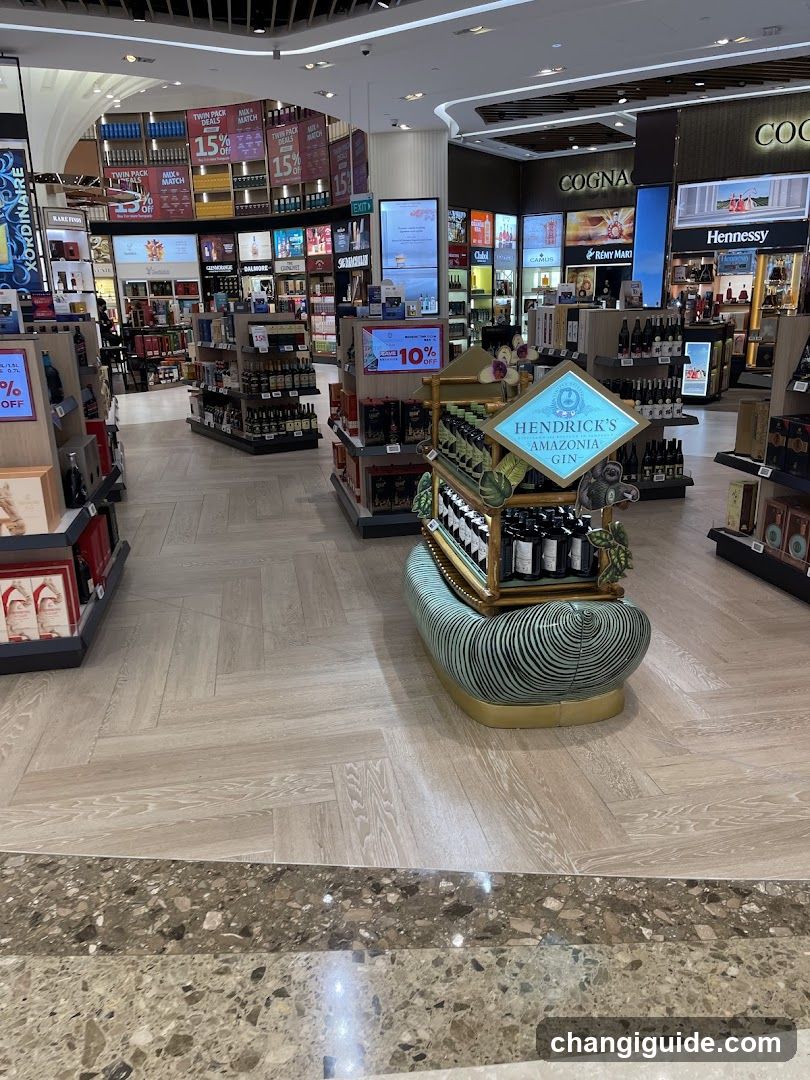 Interior view of a well-lit liquor store with wooden flooring and multiple product displays. Prominent features include a central Hendrick's Gin display on a decorative stand, surrounded by shelves stocked with various bottles. Background signage includes promotions like '15% OFF' and brand names such as Hennessy and Cogan.
