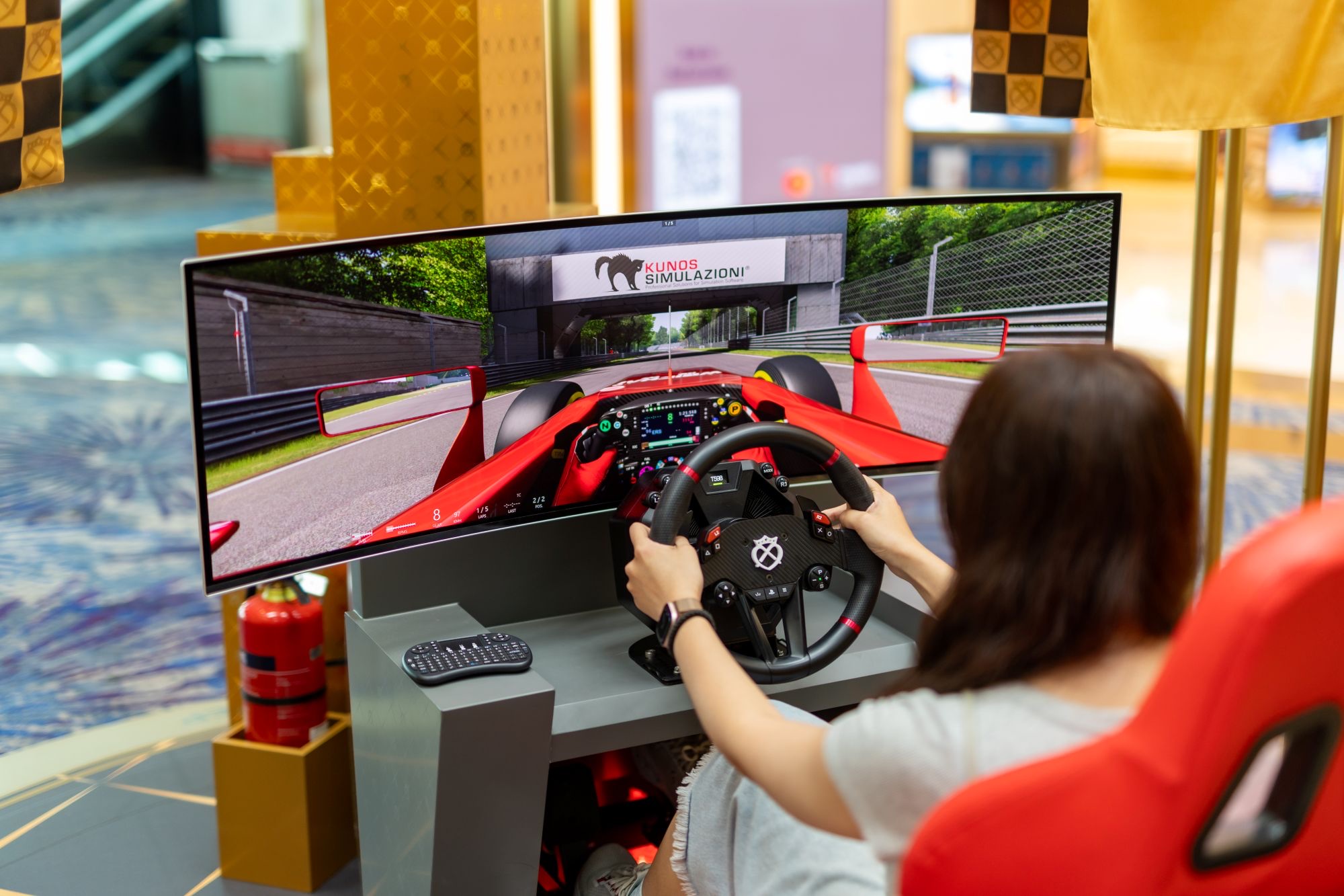 Traveller in a red seat using the Chivas Regal racing-car simulator in Changi Terminal 3 departure transit